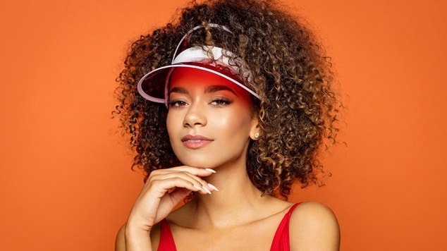 Mulher com cabelos cacheados loiro escuro e viseira, olhando diretamente para a câmera.