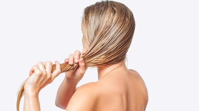 Mulher com cabelo loiro acinzentado lavando o cabelo em fundo branco.