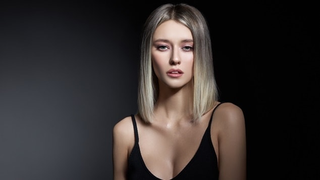 Mulher com cabelo loiro acinzentado em um fundo preto.