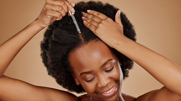 Mulher sorrindo aplicando óleo no cabelo crespo para umectação capilar.