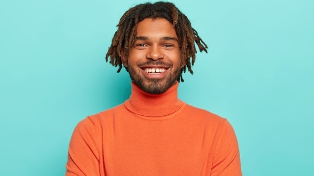 Homem sorridente com dreads curtos e camisa laranja.