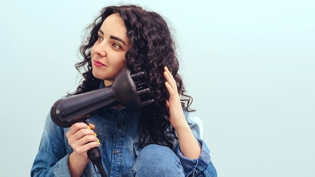 Jovem mulher utiliza um secador com difusor de cachos para definir os cachos em seu cabelo cacheado.