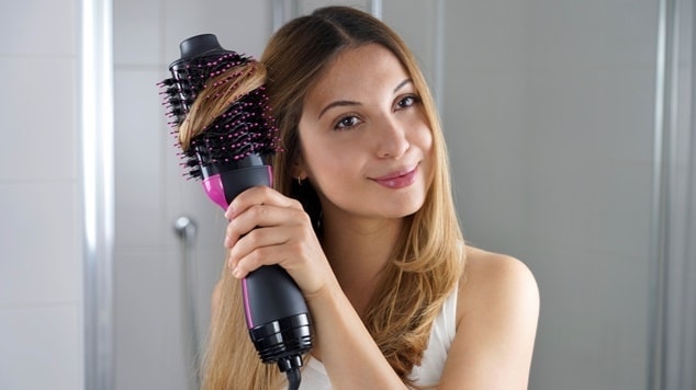 Mulher jovem utiliza escova alisadora no cabelo