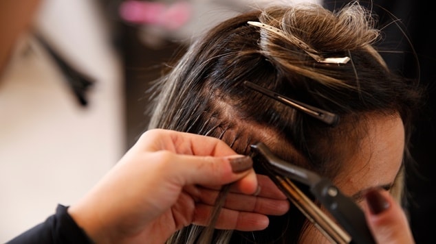 Detalhe da aplicação de mega hair com fita adesiva. Um profissional utiliza