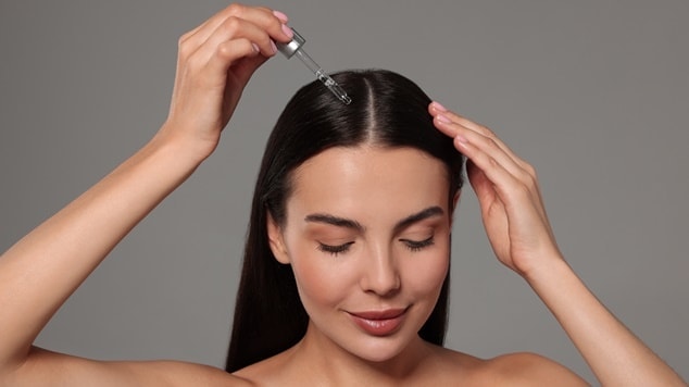 Mulher morena aplicando sérum capilar no cabelo em um fundo cinza