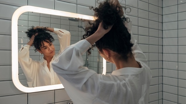 mulher com cabelo crespo curto arruma seus cachos em frente ao espelho, explorando diferentes possibilidades de penteados.