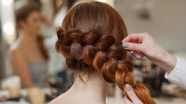 mulher com cabelo ruivo sendo trançado por uma profissional