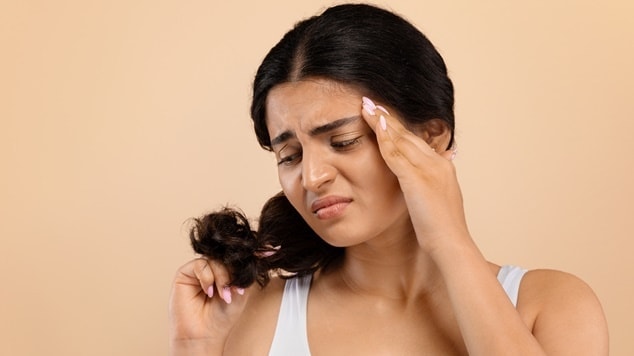 mulher com os cabelos presos demonstra frustração ao tocar em suas pontas ressecadas.