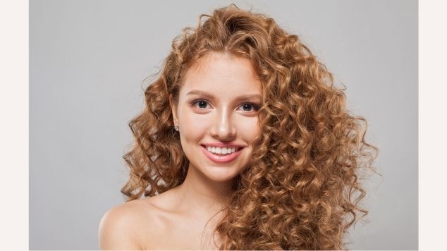 Menina sorridente com cabelo cacheado ruivo.