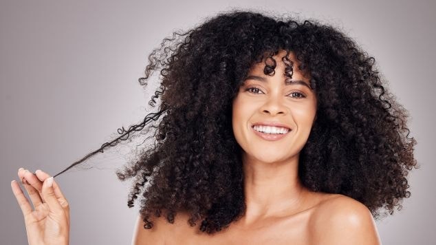 Mulher sorridente segurando um cacho com os dedos.