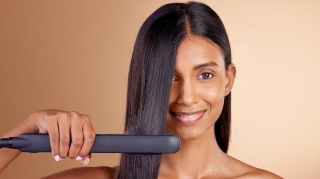 Mulher usando chapinha para alisar o cabelo, demonstrando como obter um cabelo liso e brilhante.