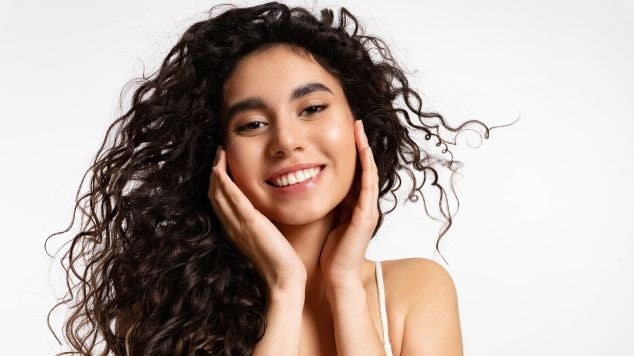 Mulher com as mãos no rosto com cabelo castanho escuro acinzentado.