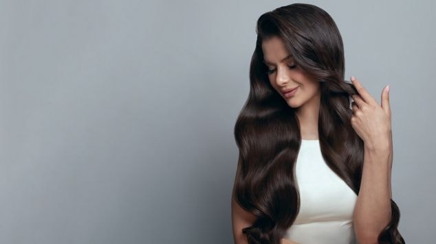 Mulher com a mão direita no cabelo castanho escuro.