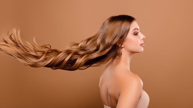 Mulher olhando para o lado direito com cabelo longo em tom loiro escuro aos ventos.