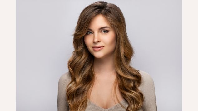 Mulher usando blusa cinza com cabelo loiro escuro dourado e maquiagem leve.