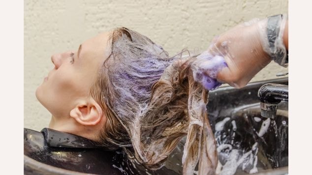 Cliente lavando seu cabelo em um salão com shampoo matizador roxo.