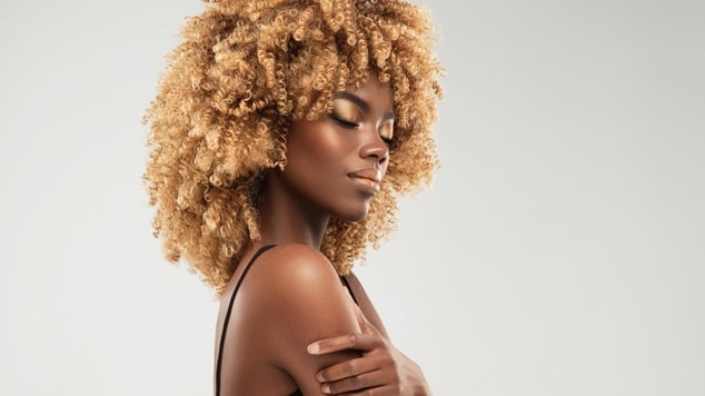Mulher negra com cabelo cacheado com tom de loiro.