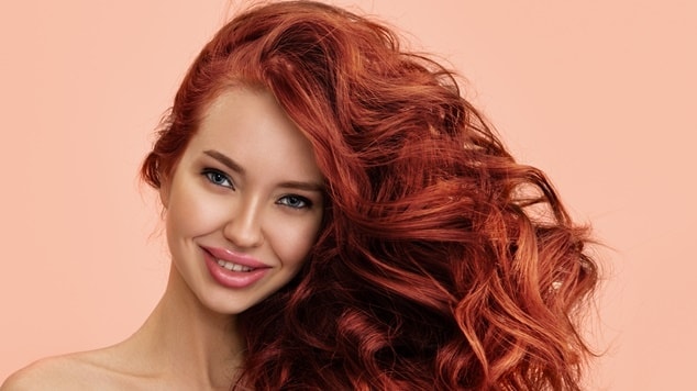 Mulher com cabelo cor carmim em fundo bege.