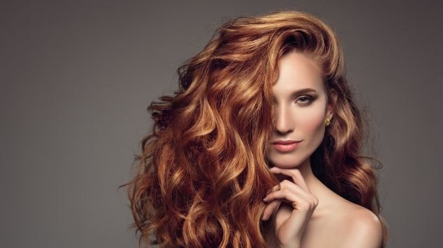 Mulher com cabelos longos e volumosos em tom ruivo doce de leite, com ondas definidas e aparência sofisticada, destacando brilho e movimento.