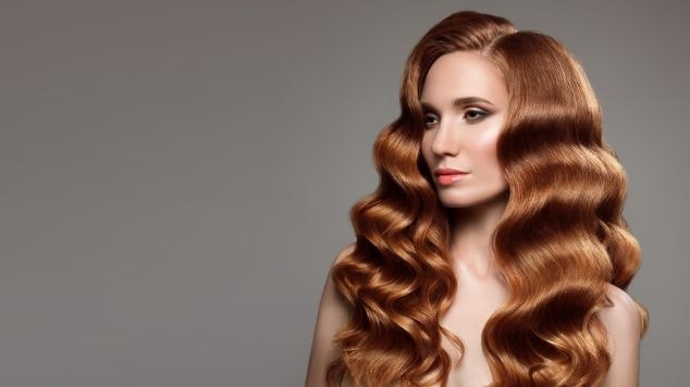 Mulher com cabelo longo com reflexos loiros olhando para o lado esquerdo com maquiagem leve.