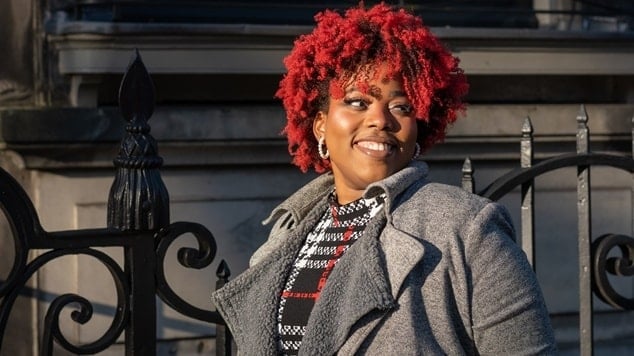 Mulher preta com tom de vermelho vibrante no cabelo cacheado.