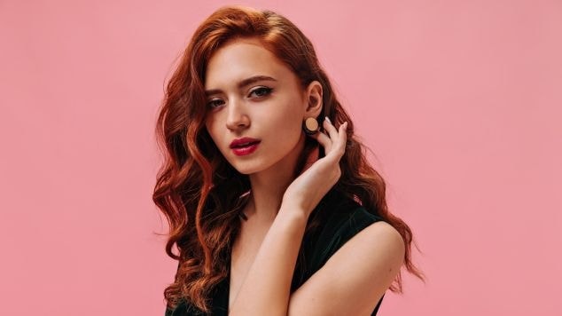 Mulher com cabelo ruivo acobreado em um fundo rosa.