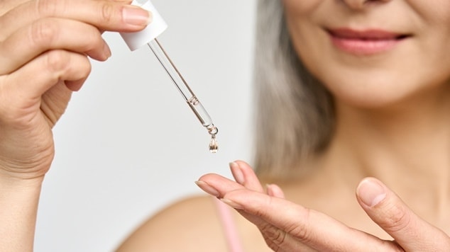 Mulher aplicando óleo capilar com conta-gotas na mão. Óleo capilar para hidratação e brilho de cabelos brancos.