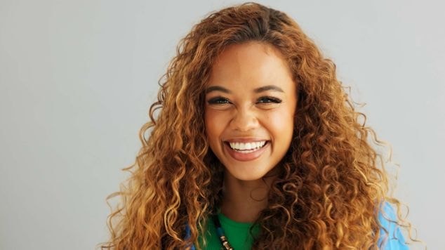 Menina sorridente com reflexos loiro mel no cabelo cacheado. 