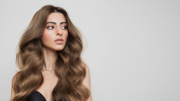 Mulher com cabelo marrom dourado em fundo cinza.