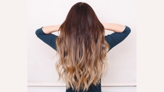 Mulher com blusa azul marinho mostrando seu cabelo com ombre hair com pontas loiras e raiz em tom castanho escuro.