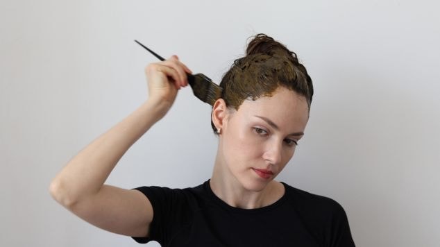 Mulher pintando a parte de trás do seu cabelo usando camiseta preta.