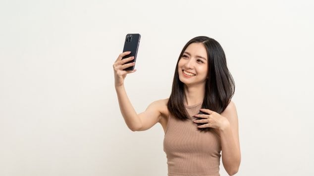 Mulher sorridente tirando uma selfie com o seu celular. 