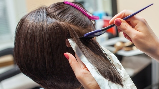 Cabeleireira pintando o cabelo de sua cliente com tinta sem amônia no salão.