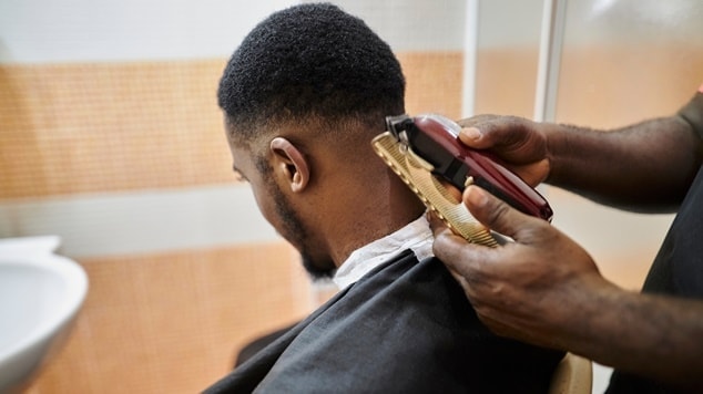 Barbeiro utilizando máquina de corte para finalizar os detalhes de um corte americano