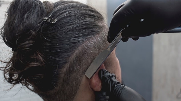 Barbeiro utilizando navalha para criar um corte americano com detalhes precisos na lateral da cabeça.