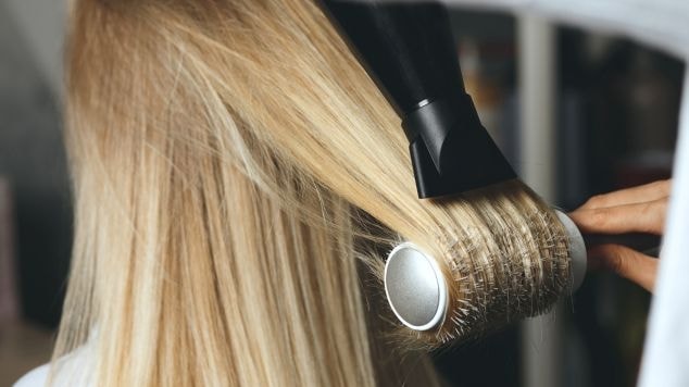 Cabeleireira escovando o cabelo loiro de sua cliente com secador e escova.