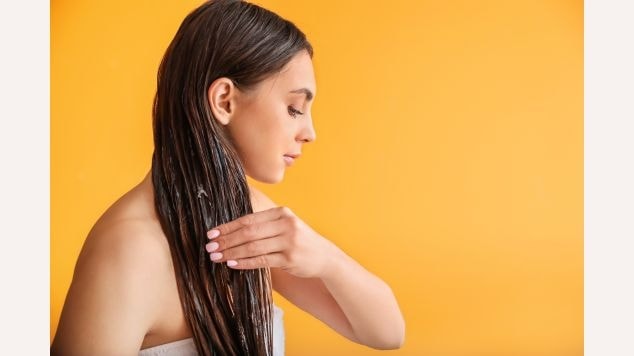 Mulher aplicando queratina em seu cabelo castanho médio em um fundo amarelo.