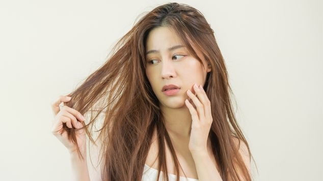 Mulher observa fios danificados e ressecados entre os dedos, com expressão de preocupação diante da falta de brilho e maciez do cabelo.