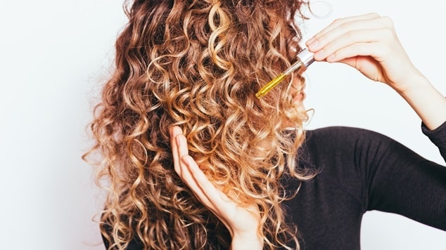 mulher aplicando óleo de argan no cabelo cacheado.