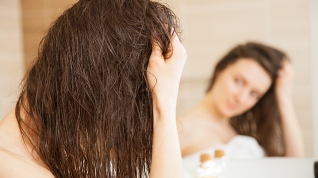 Mulher aplicando óleo de linhaça nos cabelos úmidos