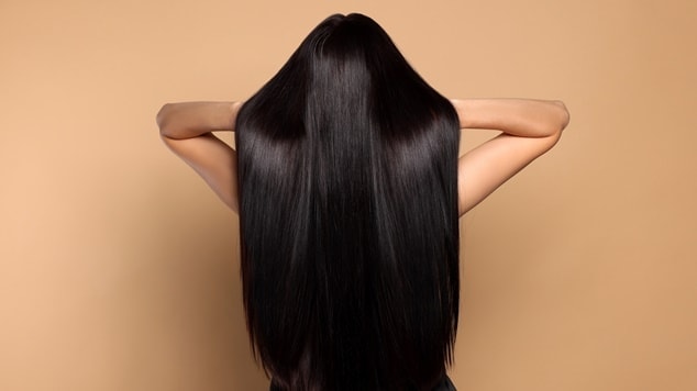 Costas de uma pessoa com longos cabelos pretos, lisos e brilhantes, sugerindo os resultados de um banho de brilho.