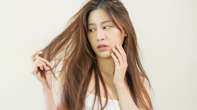 Mulher asiática com a mão no cabelo ressecado.