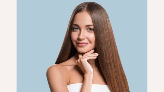 Mulher sorridente com a mão no queixo mostrando seu cabelo liso brilhante em um fundo azul.