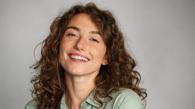 Mulher sorridente com cabelo ondulado usando blusa verde.