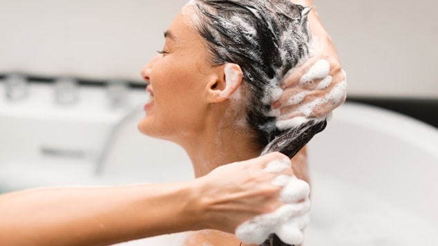 Mulher lavando o cabelo com shampoo detox no banheiro