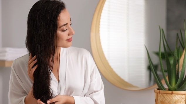 Mulher cuidando do seu cabelo usando roupão no banheiro.