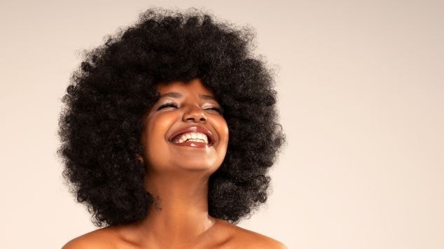 Mulher sorridente com olhos fechados e cabelos lindos e crespos volumosos e definidos.