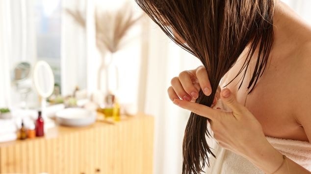 Mulher aplicando produto em seus cabelos úmidos enquanto está no banheiro.
