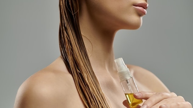 Mulher segurando um recipiente com óleo de rícino para fazer umectação capilar.