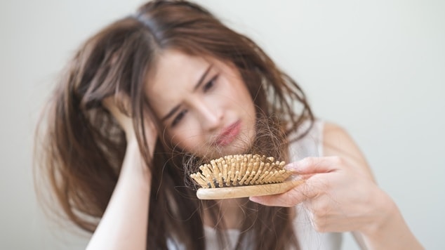 Mulher asiática segurando escova com muitos fios de cabelo devido à queda.